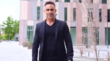 Siyah takım elbiseli mutlu bir adam yumruk tokuşturuyor, şehir ortamında başarıyı kutluyor. Kendine güveni ve vücut dili başarıyı ve motivasyonu iletir.. 