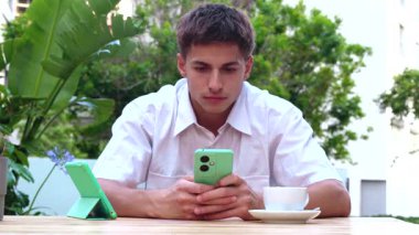 Ciddi genç adam cep telefonuna bakarak, açık kafedeki terasta mesaj yazmaya odaklanmış. Sosyal medya bağımlılığı. uygulamalar, aygıtlar teknoloji kavramı