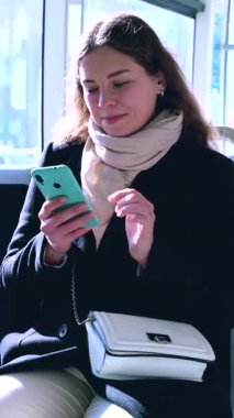 Trenle seyahat ederken akıllı telefon kullanan çekici beyaz bir kadın. Genç ve güzel bir kadın toplu taşıma araçlarını kullanıyor. Şehir ışığı tarafından aydınlatıldı. Dikey