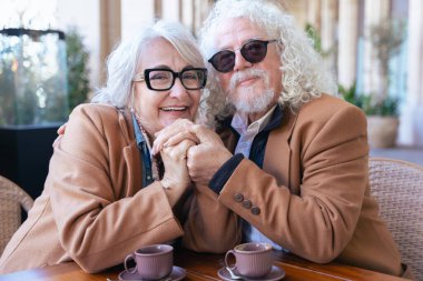Gri saçlı ve gözlüklü yaşlı bir çift bir kafede oturmuş kahvelerini içerken akıllı bir telefonu paylaşıyorlar. Birbirlerine uyumlu kahverengi paltolar giyiyorlar, gülümsüyorlar, kameraya bakarak teknolojiyi kucaklıyorlar.