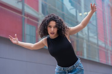 Kıvırcık saçlı, pembe ceketli, şehir ortamında hareket ve enerji ifade eden Afrikalı Amerikalı dansçı. Modern moda, çağdaş dans ve sanatsal performans.