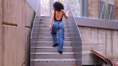 Kıvırcık saçlı, pembe ceketli, şehir ortamında hareket ve enerji ifade eden Afrikalı Amerikalı dansçı. Modern moda, çağdaş dans ve sanatsal performans.