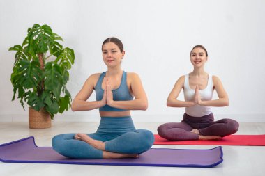 Nilüfer çiçeğinde oturan gülümseyen beyaz kadınlar dua pozisyonu almış içeride yoga minderleri üzerinde meditasyon yapıyorlar. Sağlık, farkındalık, meditasyon, barış ve sağlıklı yaşam temaları için ideal. 