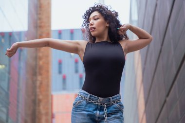 Kıvırcık saçlı, pembe ceketli, şehir ortamında hareket ve enerji ifade eden Afrikalı Amerikalı dansçı. Modern moda, çağdaş dans ve sanatsal performans.