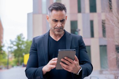 Modern bir ofis binasının dışında tablet üzerinde çalışan kendinden emin bir iş adamı. Kentsel ortam iş, teknoloji, üretkenlik ve profesyonel yaşam tarzı temaları için idealdir.