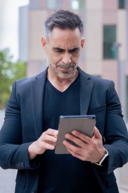Modern bir ofis binasının dışında tablet üzerinde çalışan kendinden emin bir iş adamı. Kentsel ortam iş, teknoloji, üretkenlik ve profesyonel yaşam tarzı temaları için idealdir. Dikey
