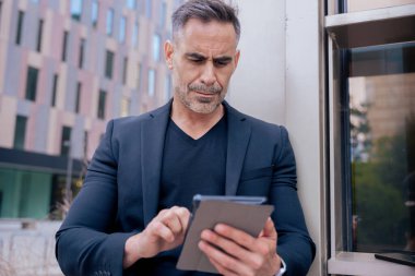 Modern bir ofis binasının dışında tablet üzerinde çalışan kendinden emin bir iş adamı. Kentsel ortam iş, teknoloji, üretkenlik ve profesyonel yaşam tarzı temaları için idealdir.