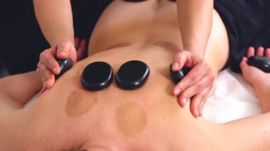 Sıcak taş masajının yakın görüntüsü, rahatlatıcı bir terapi seansı sırasında sırtüstü uzanmış siyah taşlar. Spa, sağlık, şifa ve alternatif sağlık kavramları için mükemmel.. 