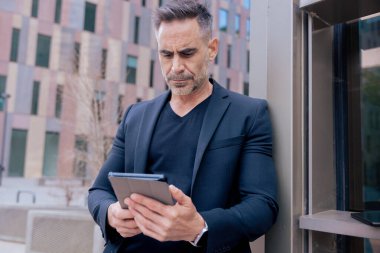 Modern bir ofis binasının dışında tablet üzerinde çalışan kendinden emin bir iş adamı. Kentsel ortam iş, teknoloji, üretkenlik ve profesyonel yaşam tarzı temaları için idealdir.