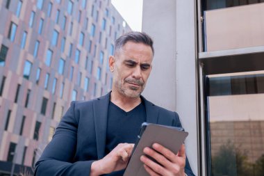 Modern bir ofis binasının dışında tablet üzerinde çalışan kendinden emin bir iş adamı. Kentsel ortam iş, teknoloji, üretkenlik ve profesyonel yaşam tarzı temaları için idealdir.