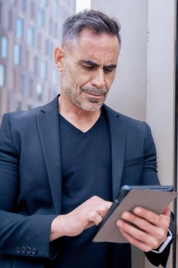 Modern bir ofis binasının dışında tablet üzerinde çalışan kendinden emin bir iş adamı. Kentsel ortam iş, teknoloji, üretkenlik ve profesyonel yaşam tarzı temaları için idealdir. Dikey