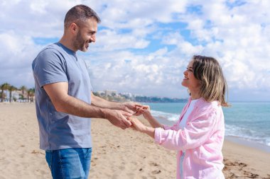 Kumsalda çıplak ayakla yürüyen, el ele tutuşan ve tatilde gülümseyen beyaz bir çift. Okyanus dalgaları, kum ve arka planda parlak bir gökyüzü olan sakin deniz kenarı anı. Boşluğu kopyala. 
