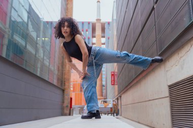 Afro-Amerikalı bir kadın şehir ortamında banklar arasında yaratıcı bir pozda dans ediyor. Günlük kıyafetler giyiyor ve denge, güç ve ifade gösteriyor. Hareket, sanat ve özgürlük kavramı. 