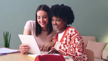 Mutlu Afrikalı Amerikalı ve Kafkasyalı öğrenciler birlikte oturup tablete bakıyorlar. Modern ortamlarda arkadaşlık, teknoloji ve öğrenme. Sosyal medyanın, eğitimin ve dijital bağlantının keyfini çıkarıyorlar.