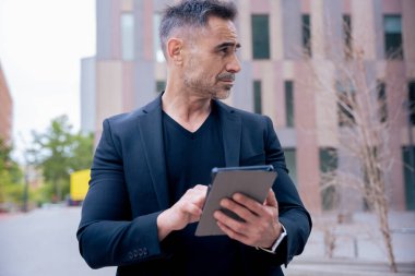 Modern bir ofis binasının dışında tablet üzerinde çalışan kendinden emin bir iş adamı. Kentsel ortam iş, teknoloji, üretkenlik ve profesyonel yaşam tarzı temaları için idealdir.