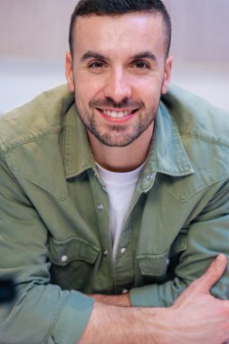 Kendine güvenen beyaz bir adamın dikey portresi, şık ve parlak bir mutfak içinde kameraya gülümseyen, rahat ve sıcak bir ev atmosferi ve görünür yiyecek ve yemek elementleri öneriyor. 