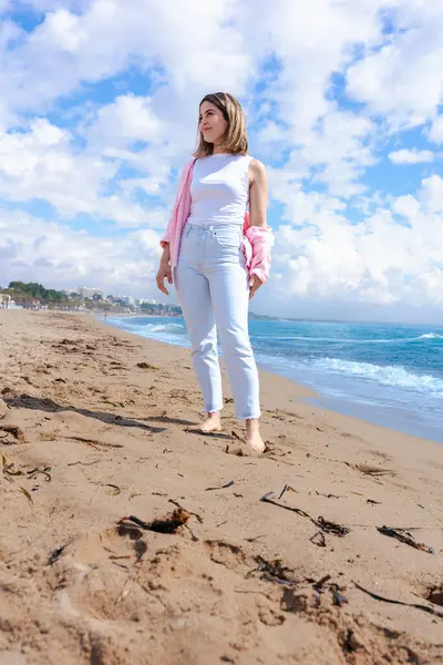 Gülümseyen genç bir kadın güneşli bir günde kumlu bir sahilde çıplak ayakla yürür. Hafif kıyafetler giyer ve etrafındaki dalgalar, mavi gökyüzü ve doğal güzelliklerle huzurlu kıyı atmosferini sever. Dikey