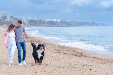 Bulutlu bir gökyüzünün altında köpekleriyle birlikte sessiz bir plaj boyunca yürüyen mutlu bir çift. Açık fotokopi alanı ve sakin bir kıyı arkaplanı olan okyanus kenarında huzurlu bir anın tadını çıkarıyorlar.. 