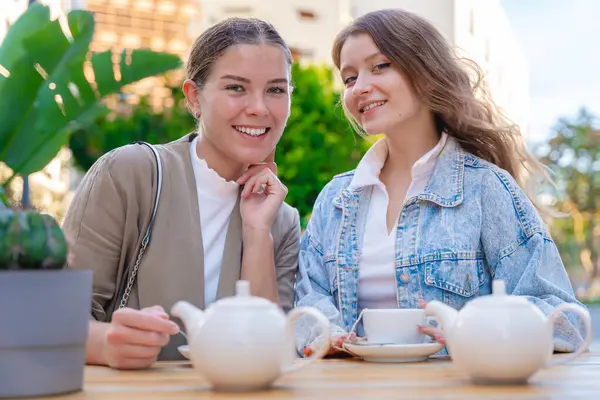 Dışarıda çay içerken gülümseyen ve kameraya bakan iki beyaz kadın portresi. Şehirde güneşli bir günde rahat ve neşeli bir arkadaşlık, rahatlık ve sohbet anı.. 
