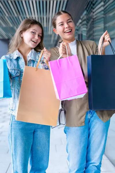 Dikey portre İki neşeli beyaz kadın kameraya bakıyor ve renkli alışveriş torbaları tutarken gülümsüyor. Açık hava ortamında neşeli ve eğlenceli alışveriş anları yakalıyorum.. 