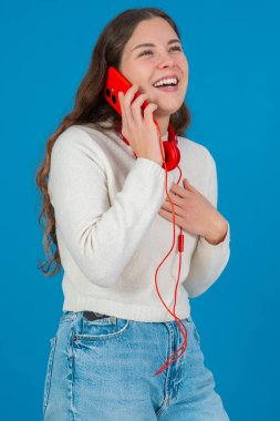 Kırmızı bir akıllı telefondan konuşan neşeli genç bir kadının dikey görüntüsü. Elini göğsüne koyup gülüyor. Parlak mavi bir arka plana yaslanıyor. Sıradan bir anda.. 