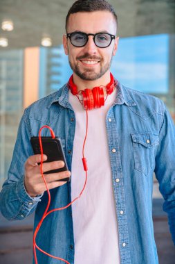 Şehir ortamında akıllı telefonunu kullanırken kırmızı kulaklıklı genç adam kahvenin tadını çıkarıyor. O okurken ya da mesajlaşırken gülümsüyor, modern cam binaların önünde sıradan bir anda duruyor. Dikey