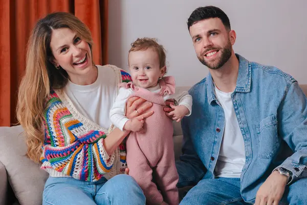 Bebekleri kanepede oturup kameraya gülümseyen mutlu ebeveynler portresi. Rahat bir ev ortamında sevgi, sıcaklık ve birliktelikle dolu sıcak aile anları.. 