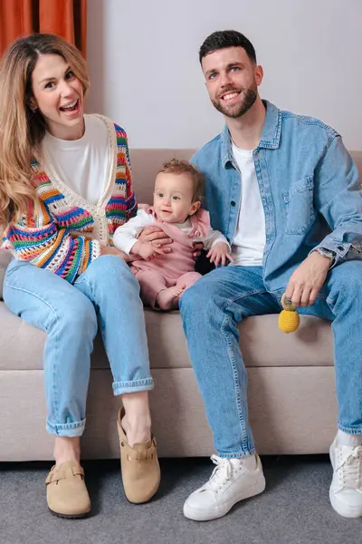 Dikey Portre Mutlu Genç Ebeveynler bebeklerini kanepeye oturtup kameraya gülümsüyorlar. Rahat bir ev ortamında sevgi, sıcaklık ve birliktelikle dolu sıcak aile anları.. 