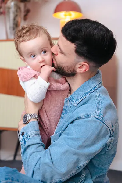 Dikey Portre Genç Baba kızını sıcak ve rahat bir evde tutarken öpüyor. Şefkatle, sevgiyle ve evde babacan sevgiyle dolu bir aile anı.. 