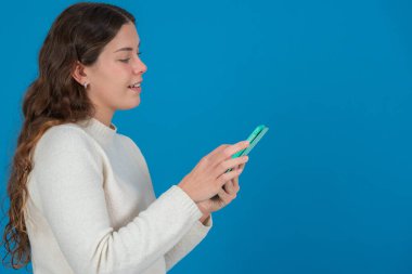 Beyaz kazak giyen gülümseyen genç bir kadının yeşil tablet kullanarak fotokopi alanındaki mavi arka plana bakması dijital iletişimi, taramayı ve teknolojik etkileşimi sembolize ediyor.. 