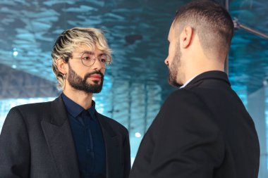 Takım elbiseli iki erkek profesyonel, yansıtıcı cam duvarları ve odaklanmış iş atmosferi olan modern bir ofis içinde ciddi bir tartışmaya giriştiler.. 