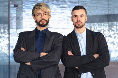 Çapraz kollu takım elbiseli iki kendine güvenen profesyonel erkek modern bir ofisin içinde kameraya karşı ciddidir. Şirket başarısı, takım çalışması ve iş ortamında liderlik.. 