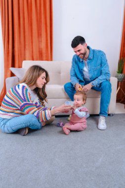 Bebeklerini beslerken yerde ve kanepede oturan genç ebeveynlerin dikey fotoğrafı. Ebeveynlik, bakım, aşk ve erken çocukluk gibi konular için ideal iç mekan ve doğal etkileşim. 