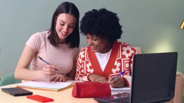 Afro-Amerikalı ve Kafkas öğrenciler evde birlikte çalışıyorlar, dizüstü bilgisayar kullanıyorlar ve not alıyorlar. Kırtasiye ve kitaplarla modern bir çalışma alanında ortak öğrenim, takım çalışması ve eğitim.