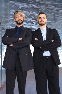 Dikey portre. Çapraz kollu iki kendine güvenen erkek profesyonel modern bir ofisin içinde kamera karşısında ciddi duruyor. Şirket başarısı, takım çalışması ve iş ortamında liderlik.. 