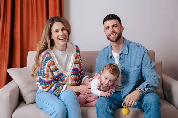 Bebekleri kanepede oturup kameraya gülümseyen mutlu ebeveynler portresi. Rahat bir ev ortamında sevgi, sıcaklık ve birliktelikle dolu sıcak aile anları.. 