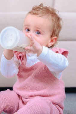 Evde otururken süt şişesini tutan ve içen bir kızın yakın plan görüntüsü. Hassas çocukluk anı, ebeveynlik, beslenme, büyüme ve erken gelişim temaları için idealdir. Dikey