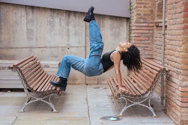 Afro-Amerikalı bir kadın şehir ortamında banklar arasında yaratıcı bir pozda dans ediyor. Günlük kıyafetler giyiyor ve denge, güç ve ifade gösteriyor. Hareket, sanat ve özgürlük kavramı. 