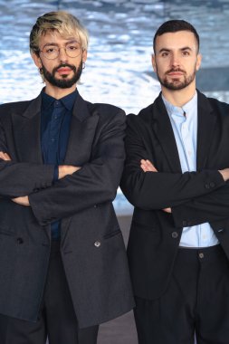 Dikey portre. Çapraz kollu iki kendine güvenen erkek profesyonel modern bir ofisin içinde kamera karşısında ciddi duruyor. Şirket başarısı, takım çalışması ve iş ortamında liderlik.. 