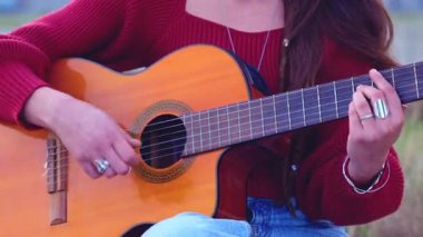 Akustik gitar çalan ve deniz kenarında şarkı söyleyen tanınmayan genç sanatçı. Doğayla ve yumuşak doğal ışıkla çevrili sakin bir sahil ortamında duygusal bir performans sergiliyor.. 