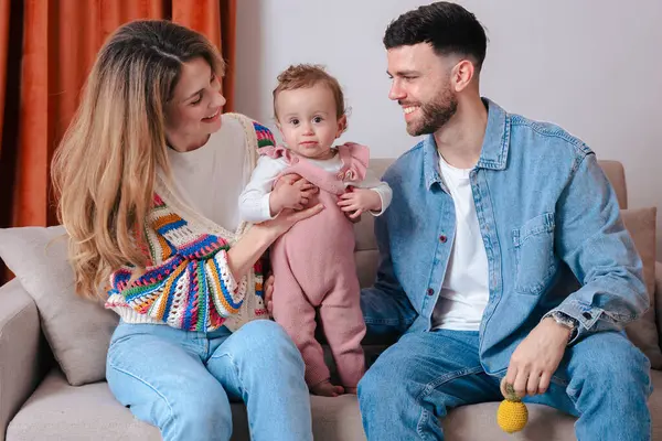 Kanepede oturup gülümseyen ve rahat bir anın tadını çıkaran genç ebeveynler. Sıcak aile sahnesi neşe, sevgi ve aile bağlarıyla dolu.. 