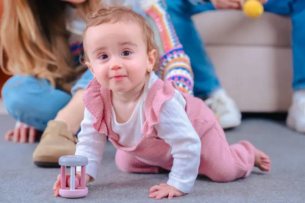 Sevimli bebek halıda sürünüyor kameraya gülümsüyor, neşe ve merak gösteriyor. Annem yerde arkada oturuyor. Sıcak ve doğal ışıkla dolu tatlı bir aile anı.. 