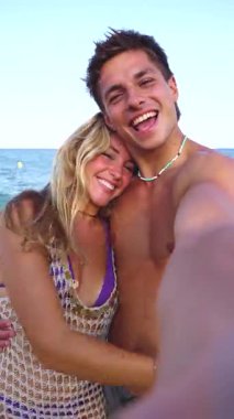 Gülümseyen etnik çeşitlilikte bir kadın ve tatilden zevk alan bir erkek. Güzel ve neşeli bir çift z nesli cep telefonlu fotoğraf için poz veriyor. Dikey