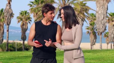 Atletik çift birbirine sarılıyor ve neşeli bir selfie çekiyor. Deniz kenarındaki yemyeşil bir palmiye bahçesinde kırmızı bir akıllı telefon ile yaz aşkını, sporu, seyahat anılarını ve canlı açık hava yaşam tarzını kutluyorlar..