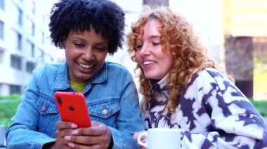 Açık bir kafede iki farklı arkadaş nefes nefese kutlama yapıyor ve kırmızı bir akıllı telefona bakarken şaşkınlıklarını paylaşıyor, şehirde kahve eşliğinde tezahürat yapıyor ve kaynaşıyorlar. Dijital haberler öğleden sonralarını aydınlatıyor.. 