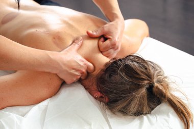 Masaj terapistinin elleri, müşterilerine nazikçe baskı uyguluyor. Beyaz masaj masasının üst sırtına. Kapalı alanda, kas gevşemesi ve sağlıklı bir spa ortamında. 