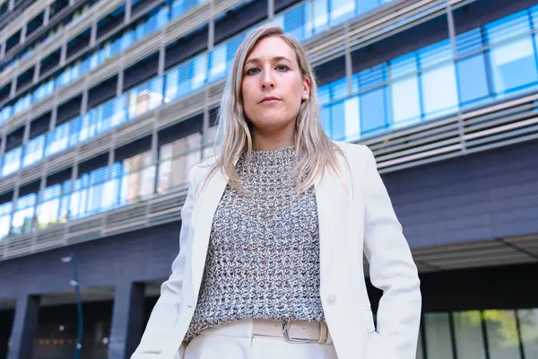 Hafif bir takım elbise giyen, ciddi şekilde kameraya bakan, modern bir ofis binasının önünde duran, liderliği, kararlılığı ve profesyonelliği temsil eden kendine güvenen bir iş kadını.. 