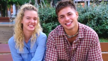 Genç bir adam ve kadın parkta otururken kameraya gülümsüyor, günlük kıyafetler, doğal ışık, dostane ruh hali, sosyal medya konsepti, açık hava yaşam tarzı, seyahat, hafta sonu keyfi, kopyalama alanı. 