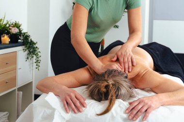 Masaj terapistinin elleri, müşterilerine nazikçe baskı uyguluyor. Beyaz masaj masasının üst sırtına. Kapalı alanda, kas gevşemesi ve sağlıklı bir spa ortamında. .