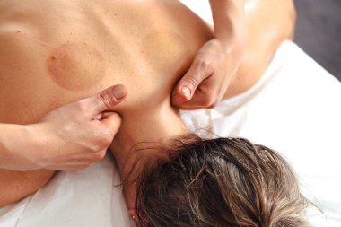 Masaj terapistinin elleri, müşterilerine nazikçe baskı uyguluyor. Beyaz masaj masasının üst sırtına. Kapalı alanda, kas gevşemesi ve sağlıklı bir spa ortamında. 